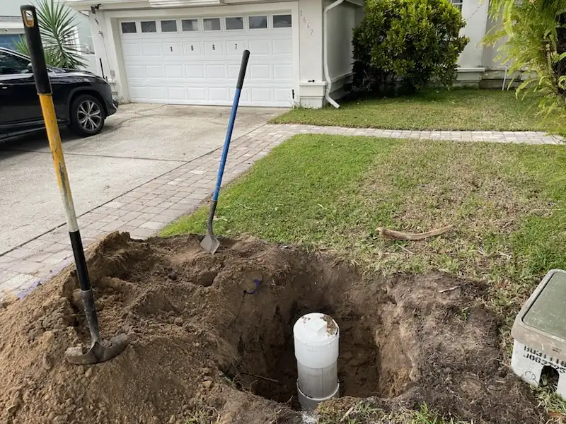 Hand excavated hole with a vertical PVC cleanout pipe installed near a driveway