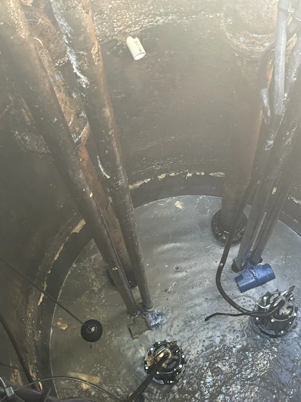 Looking down into a concrete lift station wet well showing guide rails and submersible pumps