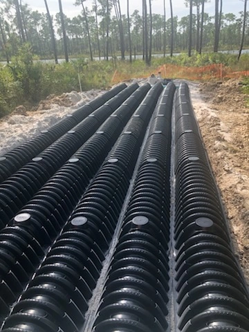 Rows of black plastic infiltrator chambers laid out for a septic drain field installation in sandy soil