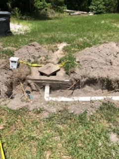 Partially excavated concrete septic tank with white PVC outlet pipe in a residential yard