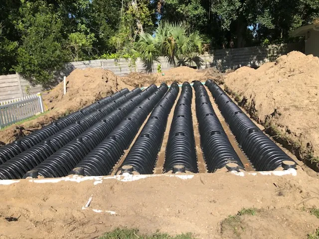 Large array of black plastic septic drain field chambers installed in a sandy trench