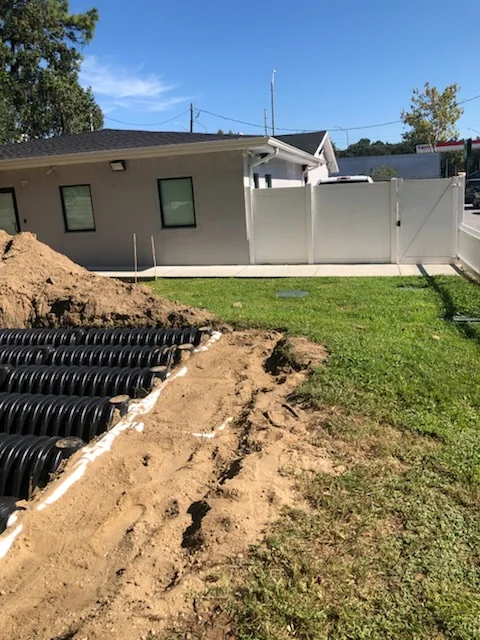 Septic drain field installation next to a building and white fence with green septic tank access lids visible