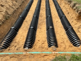 Close-up of four parallel rows of black septic drain field chambers and a green distribution pipe in a sandy trench