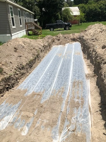 Three rows of septic drain field chambers covered with grey geo-textile filter fabric in a sandy trench