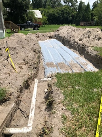White PVC distribution pipe connecting to a newly installed septic drain field covered in filter fabric