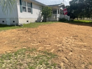 Freshly graded dirt covering a newly installed septic drain field next to a residential home with a covered porch