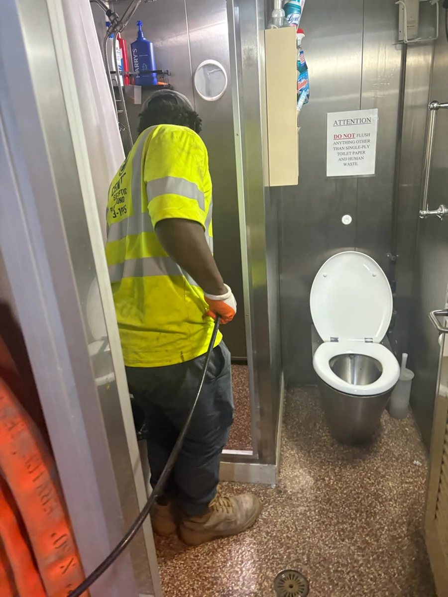 Technician running a jetter hose through a narrow stainless steel crew head aboard a cutter with a fire hose station behind him
