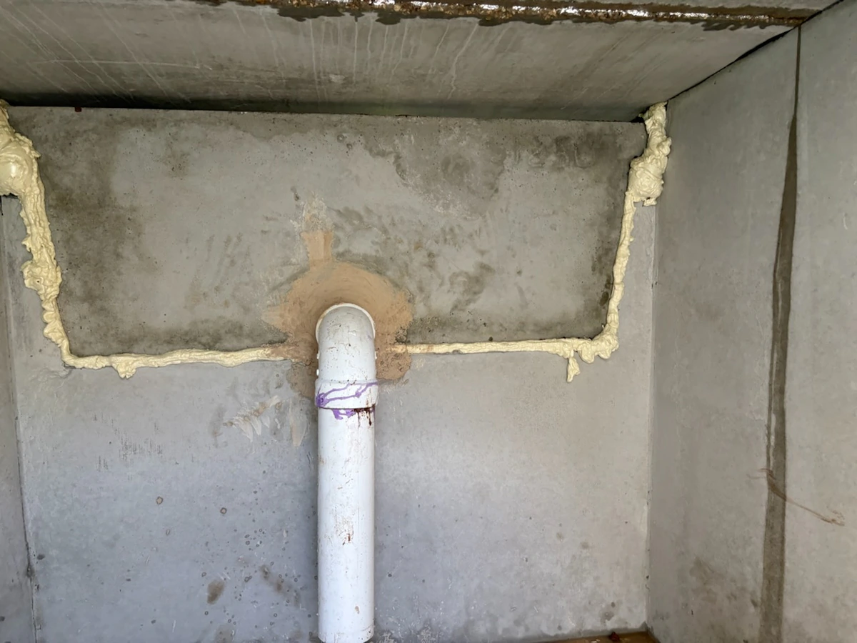 Inside a new grease interceptor showing the inlet pipe grouted through the concrete wall and sealant run along the baffle joint