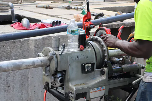 Close view of a power threading machine cutting threads on galvanized pipe beside a concrete basin