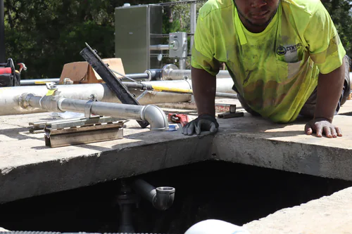 Technician kneeling at a basin opening lining up a new elbow with the pipe below