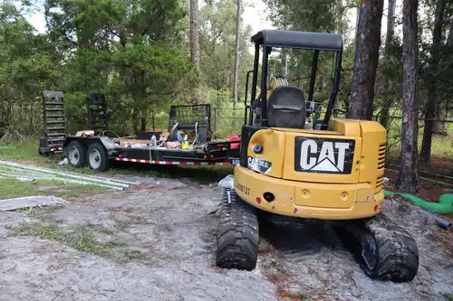 Compact excavator and equipment trailer staged on sand at the park job site