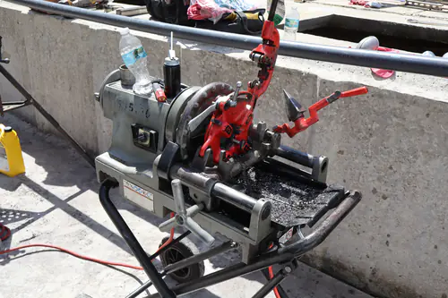 Pipe threading machine with its cutter and reamer set up on a stand next to the plant wall
