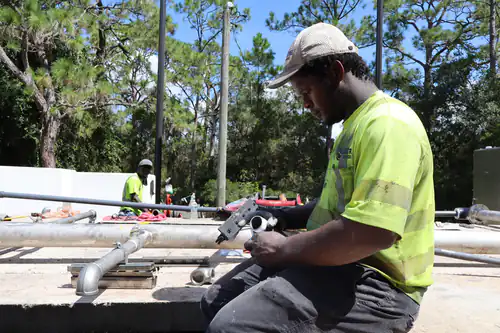 Technician seated on the basin wall finishing a taped galvanized fitting