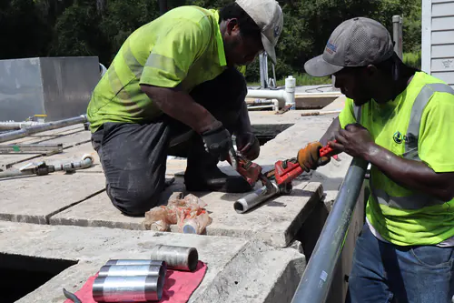 Two technicians using pipe wrenches to assemble galvanized nipples on top of the basin