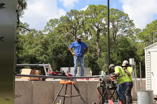 Supervisor standing on the basin wall watching two technicians thread pipe below
