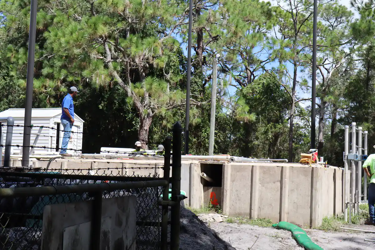 Fenced park wastewater plant in Orlando with concrete treatment basins, a chlorine shed, and a green sediment sock along the fresh excavation