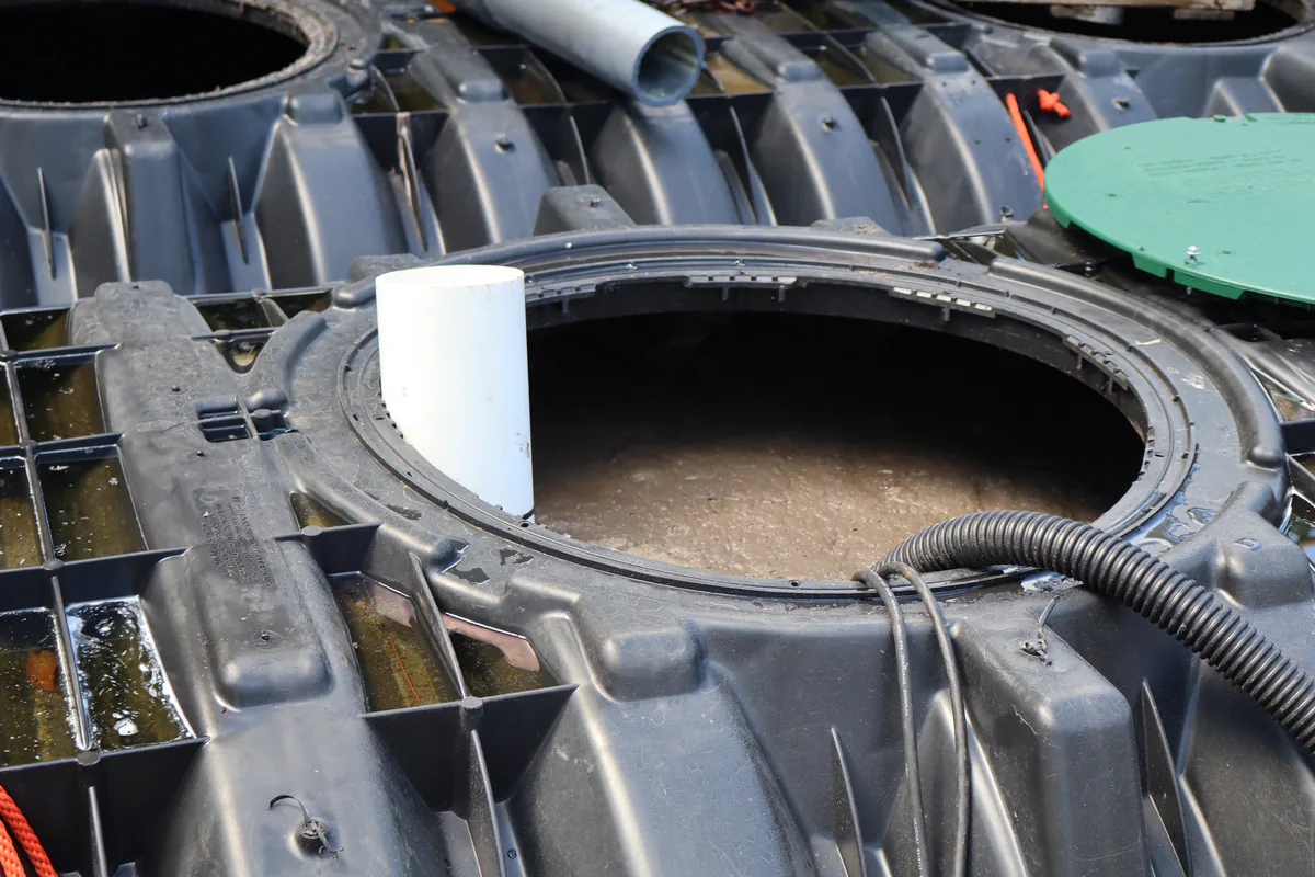 Open access riser on a black plastic septic tank showing the liquid level inside, with the green lid set aside